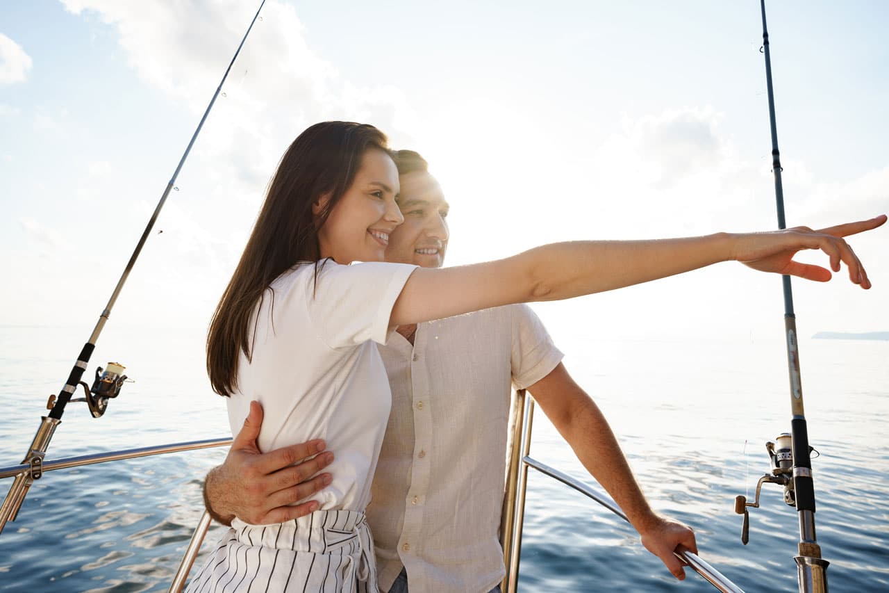 A couple embracing and pointing toward the horizon on a peaceful ocean during a romantic whale watching cruise, perfect for Valentine’s Day.
