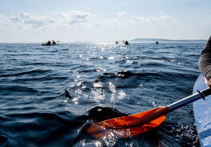 Kayak goes on a clear lake with sunshine on the background of a